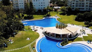 Une grande piscine à la forme incurvée, entourée de pelouse et d’arbres, avec un espace abrité et des chaises longues.