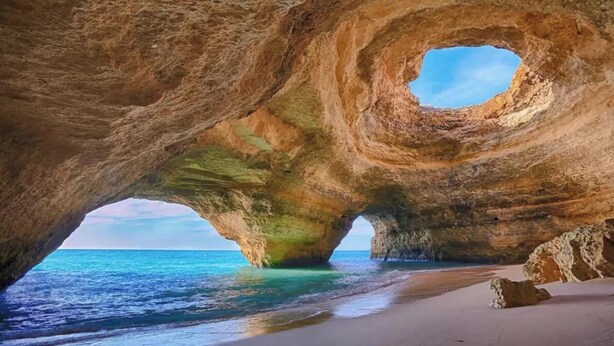 Une formation rocheuse naturelle présentant une ouverture circulaire, une plage et la mer.