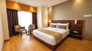 A hotel room with a large bed, a desk, two chairs, a wooden floor, and a window with curtains. - Sumitel Vista 800m from Mall Road (Darjeeling)