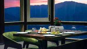 A dining table set with plates, cutlery, and a vase of flowers, with a mountain view through a window. - Sumitel Vista 800m from Mall Road (Darjeeling)