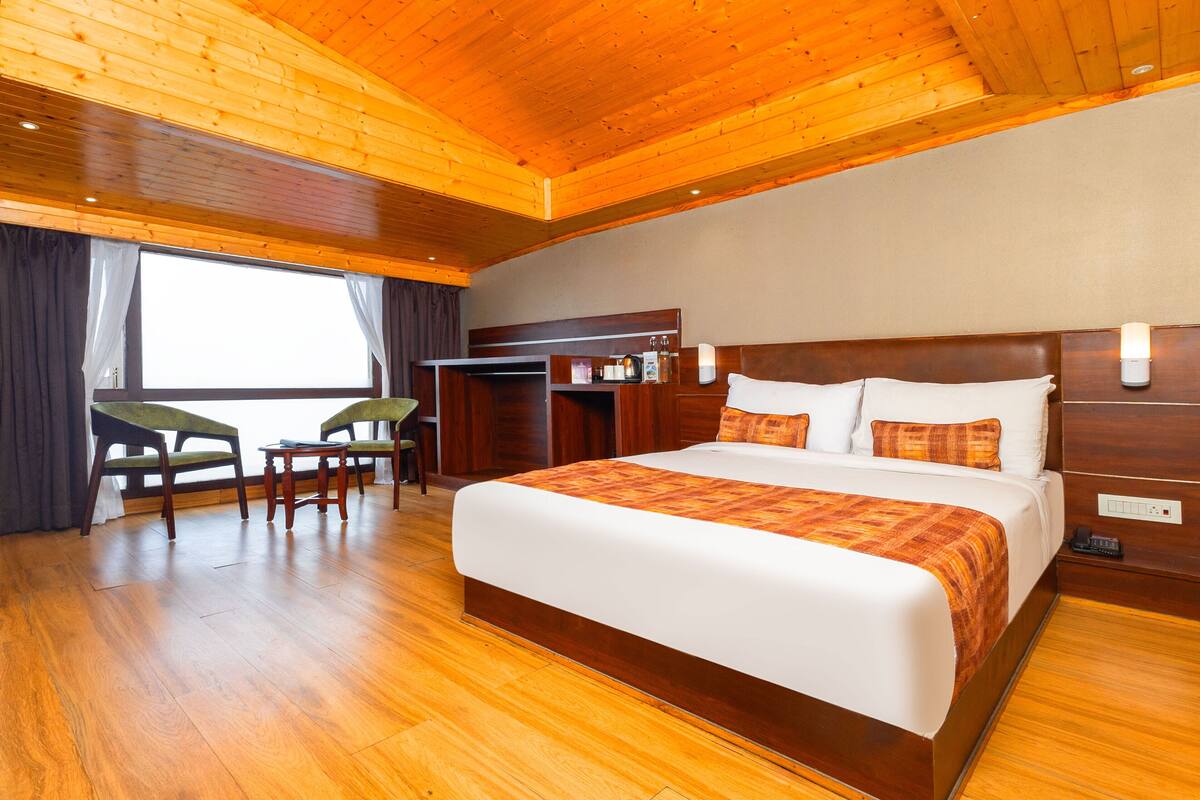 A spacious bedroom with a large bed, wooden floor, a desk, and a chair.