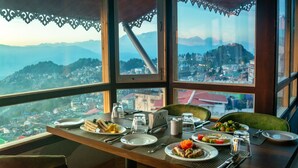 A dining table set with plates, cutlery, and glasses, overlooking a mountainous landscape through large windows. - Sumitel Vista 800m from Mall Road (Darjeeling)