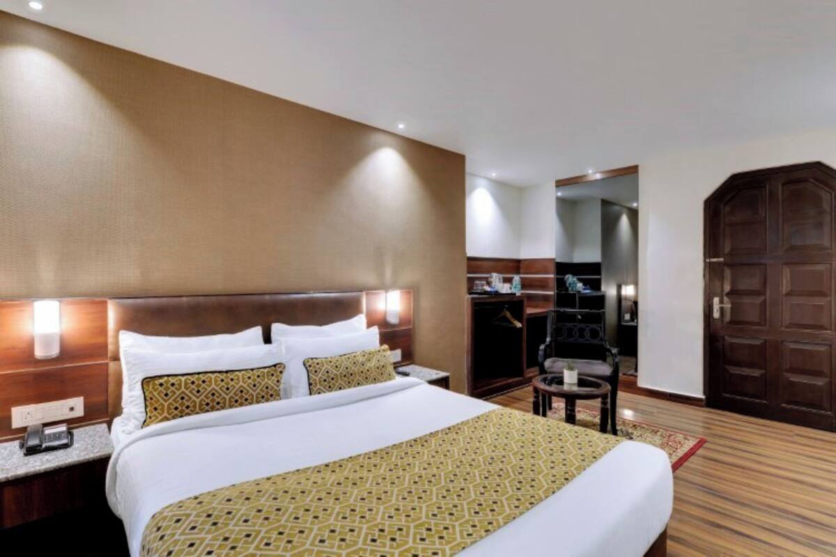 A hotel room with a large bed, a wooden headboard, a nightstand, a desk, a chair, and a wardrobe.