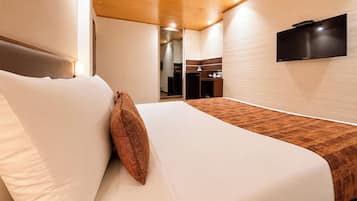 A hotel room with a bed, a television mounted on the wall, and a wooden floor.