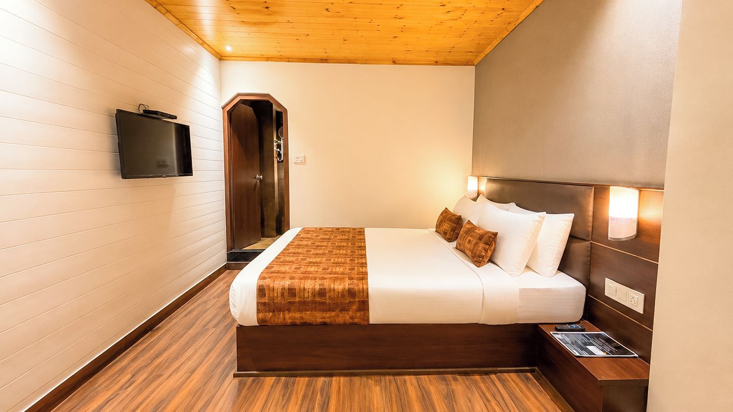 A hotel room with a bed, a flat-screen TV mounted on the wall, and a wooden ceiling.
