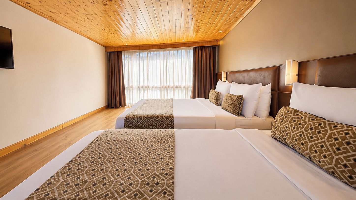 Una habitación de hotel con dos camas, techo de madera, un ventanal grande con cortinas y un televisor de pantalla plana.