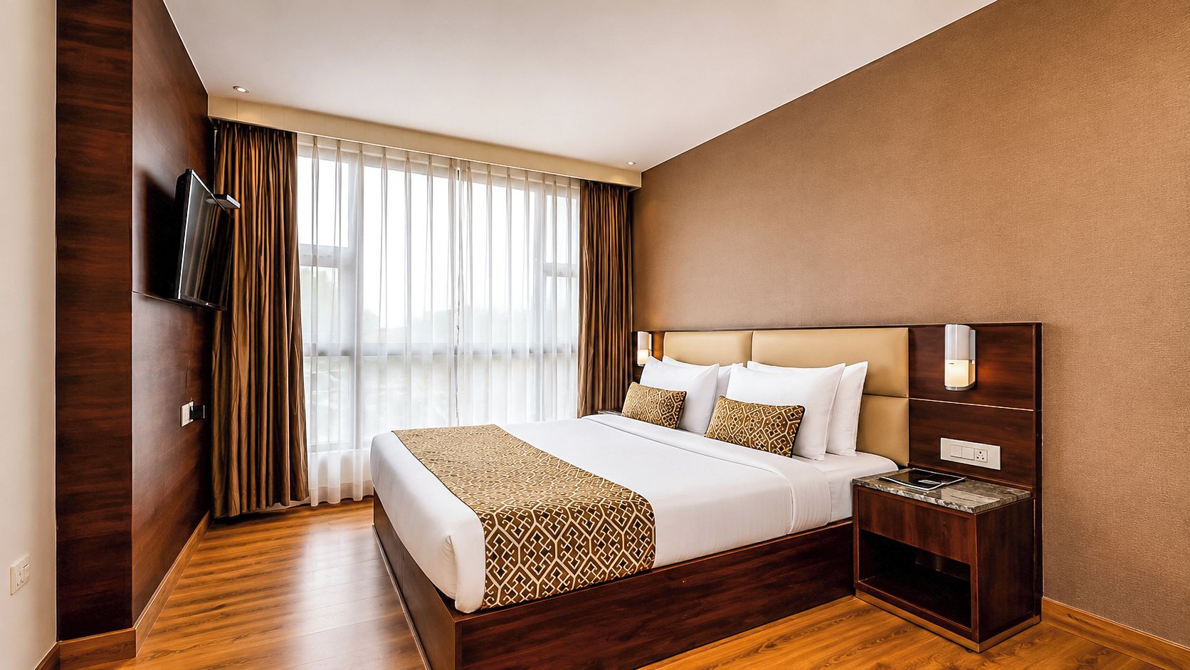 Een hotelkamer met een groot bed, een nachtkastje, een flatscreen televisie en een raam met gordijnen.