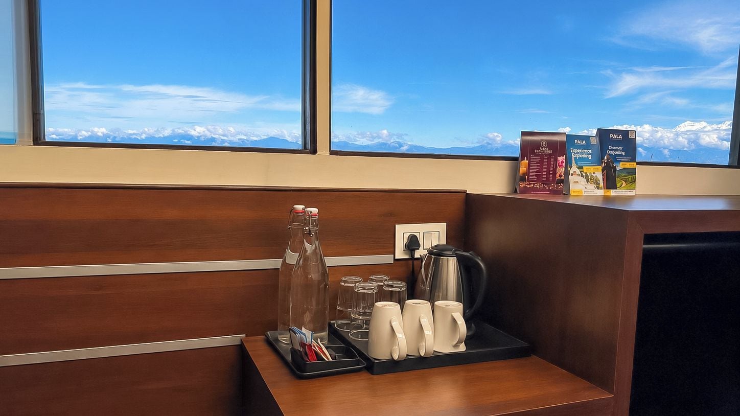 Un mostrador de recepción de hotel con una estación de café, que incluye una cafetera, tazas y una bandeja con una botella y vasos.