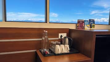 Un mostrador de recepción de hotel con una estación de café, que incluye una cafetera, tazas y una bandeja con una botella y vasos.