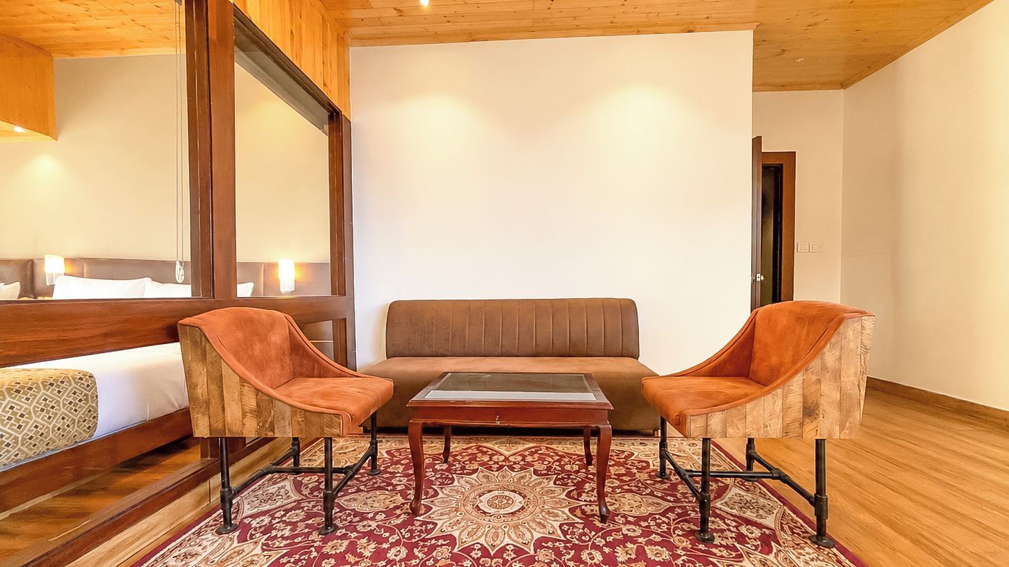 Una habitación con una cama, dos sillones, un sofá, una mesita de centro y una alfombra estampada.