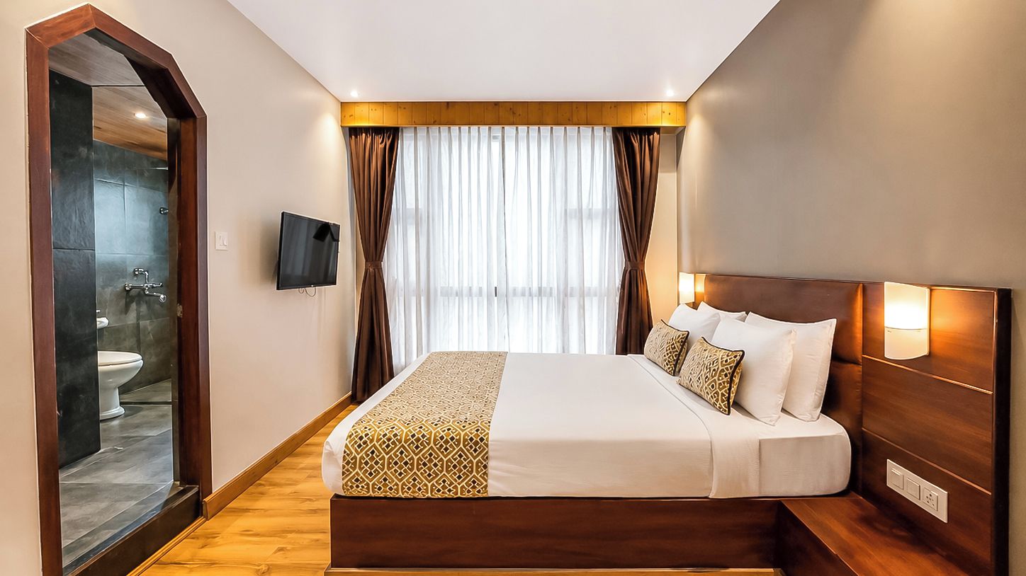 A hotel room with a large bed, a wooden headboard, a television, and a view of the bathroom.
