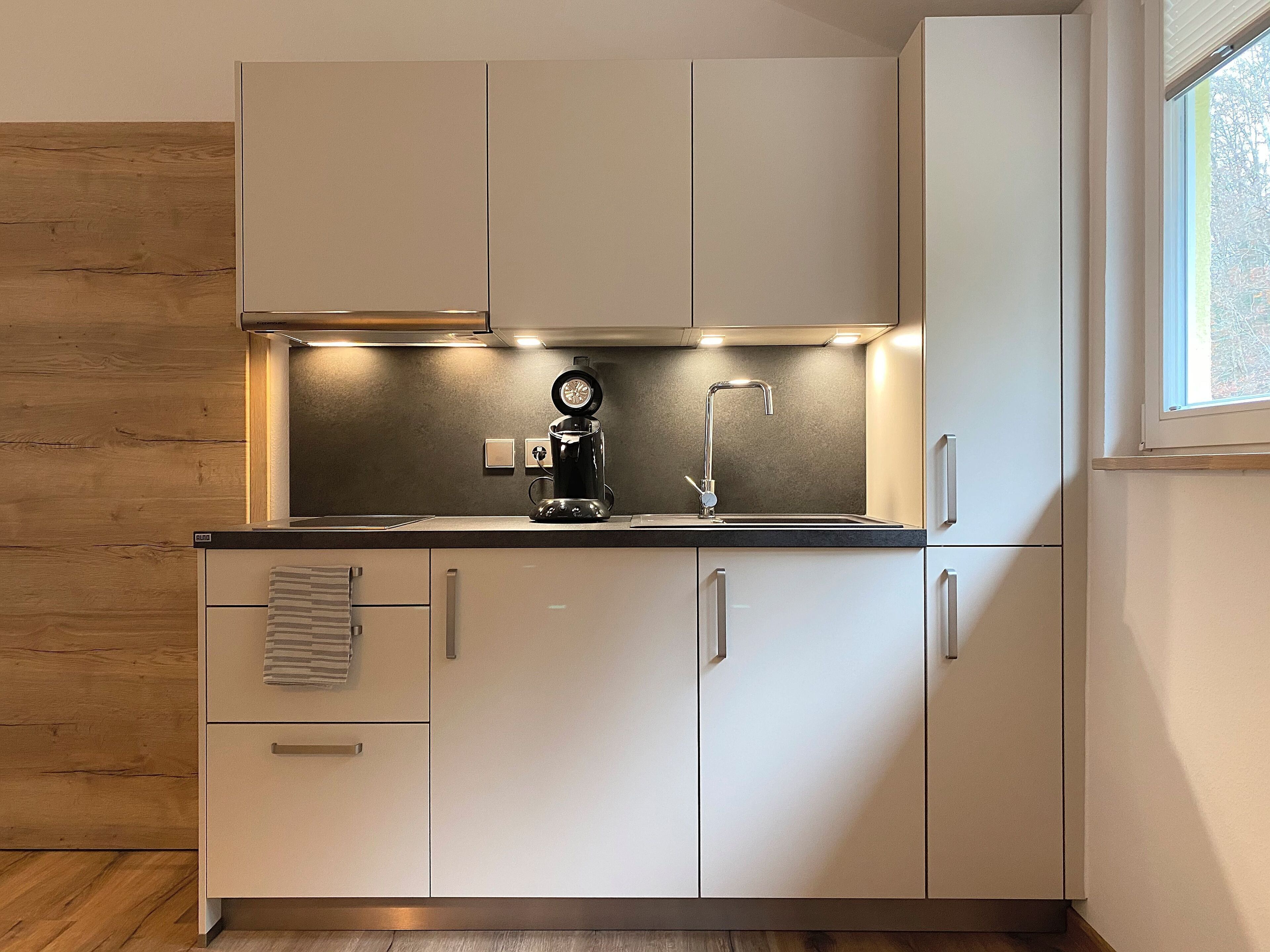 A modern kitchen with white cabinets, a black coffee maker, and a window providing natural light.
