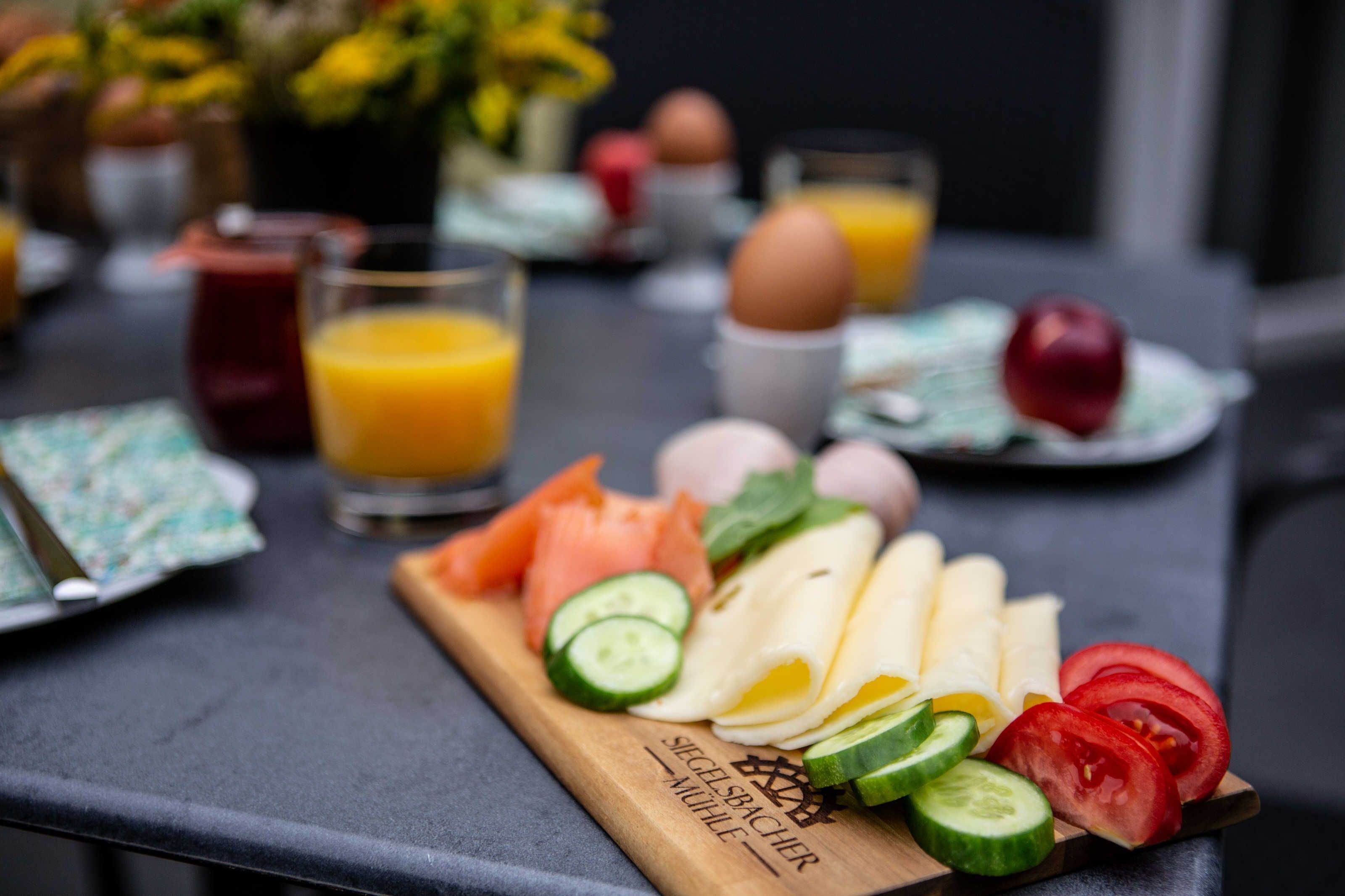 Ein Frühstücksbuffet mit Obstscheiben, Gemüse, Eiern und Räucherlachs auf einer Holzplanke.