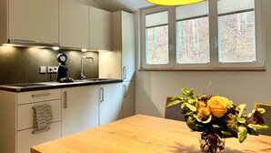 Une cuisine moderne avec des meubles blancs, un plan de travail noir et une table à manger en bois. Un vase rempli de fleurs est posé sur la table.