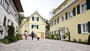 Une ruelle pavée bordée de bâtiments traditionnels aux volets verts, avec un bâtiment central doté d’un toit en pente.