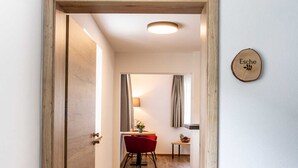 Un couloir au plancher de bois menant à une salle à manger où se trouvent une chaise et une table rouges.