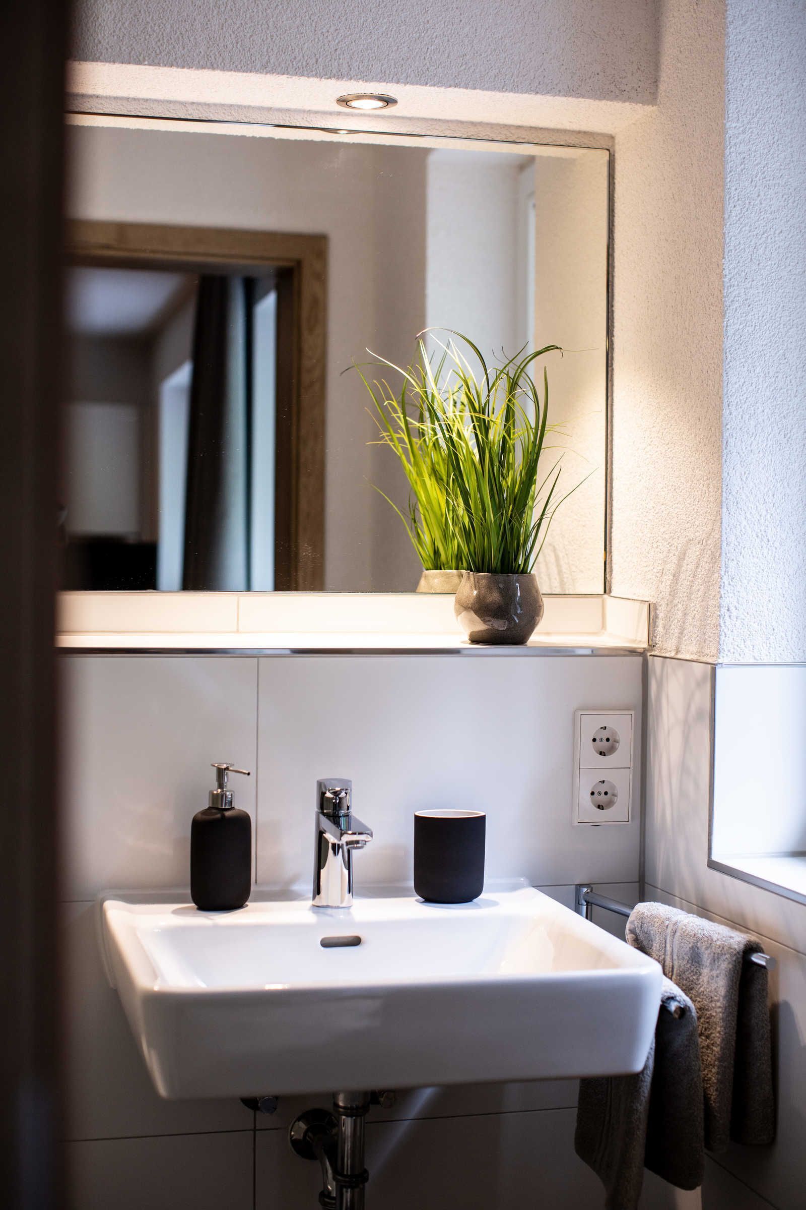 A bathroom with a white sink, a mirror, a potted plant, and a towel rack.