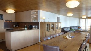 A modern kitchen with wooden cabinets, a central island, and a dining area with a long table and chairs.