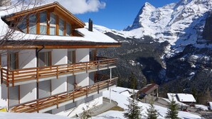 A wooden chalet with a balcony overlooking a snowy mountain landscape.