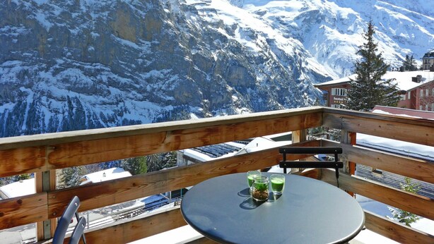 A balcony with a table and chairs overlooking a snow-covered mountain range.
