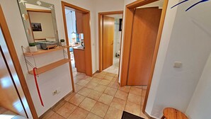 A hallway with a kitchen area, a dining table, and a bathroom visible through an open door. - Wohnung 01 EG - Villa Adebar (Heringsdorf)