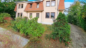 A two-story house with a brick roof, surrounded by greenery and a paved driveway. - Wohnung 01 EG - Villa Adebar (Heringsdorf)