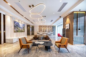 Hall d'albergo moderna con pavimento in marmo, divano, due poltrone, un tavolino da caffè e un lampadario decorativo.