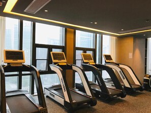 Un gimnasio con cintas de correr alineadas contra una pared con ventanas amplias.