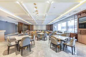 Una sala conferenze spaziosa con numerosi tavoli e sedie, un moderno design del soffitto e un'ampia finestra che permette l'illuminazione naturale.