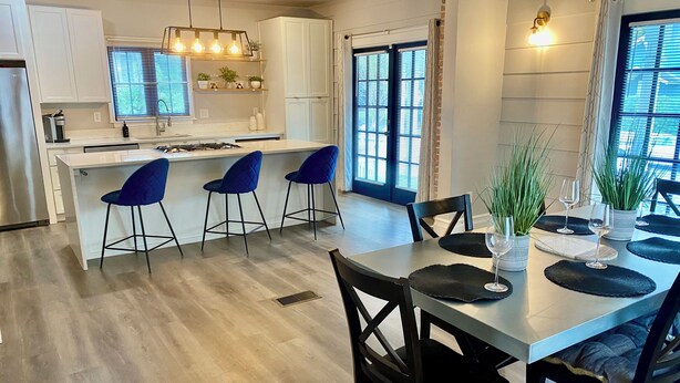 A modern kitchen with white cabinets, a central island with bar stools, and a dining area with a table set for two. - Historic Main House Retreat (Orlando)