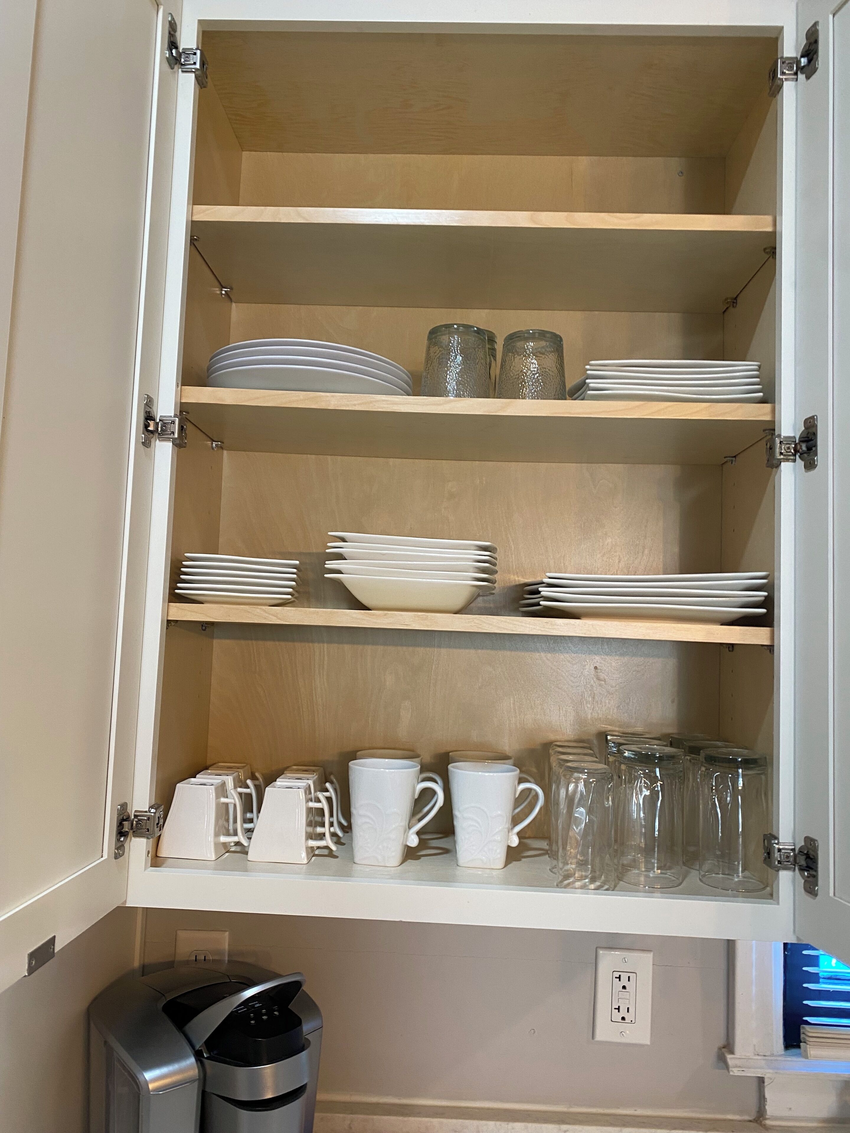 A kitchen cabinet with shelves holding plates, bowls, and glassware.