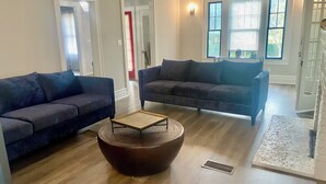 A spacious living room with two dark sofas, a round coffee table, and a large window providing natural light. - Historic Main House Retreat (Orlando)
