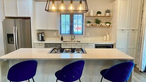 A modern kitchen with a central island, white cabinets, a stainless steel refrigerator, a gas stove, and three blue bar stools. - Historic Main House Retreat (Orlando)