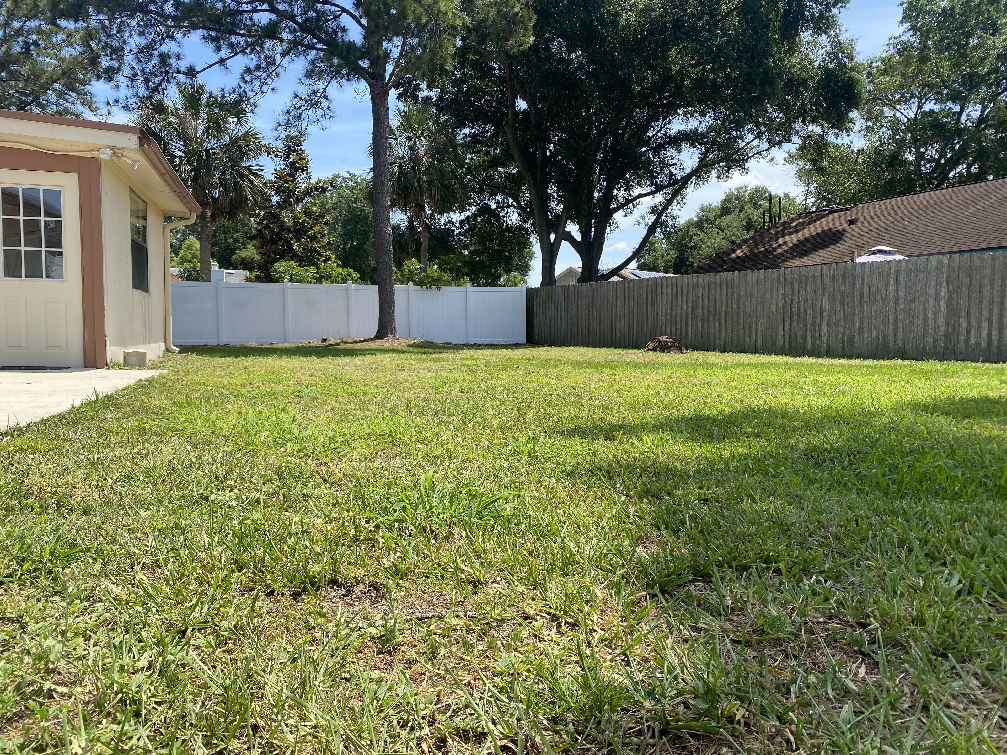 A backyard with a lawn, a white fence, and a building with a brown door and windows.