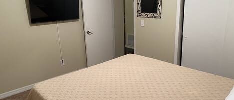 Un dormitorio con cama, televisor montado en la pared y dos puertas.