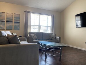 A living room with a sofa, a glass coffee table, and a TV mounted on the wall.