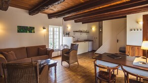 A cozy living room with a sofa, wicker chairs, and a dining table. A kitchen is visible in the background with a white refrigerator and a sink. - Domaine Leyvinie, gite Syrah, 10 minutes from the Dordogne (Perpezac-le-Blanc)