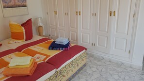 Een net opgemaakt bed met een kleurrijke quilt, een bedlamp en een stapel opgevouwen handdoeken.