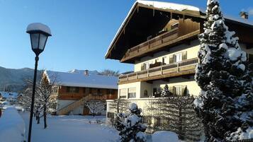 Ein zweistöckiges Gebäude mit Balkon, umgeben von schneebedeckten Bäumen und wolkenlosem Himmel.
