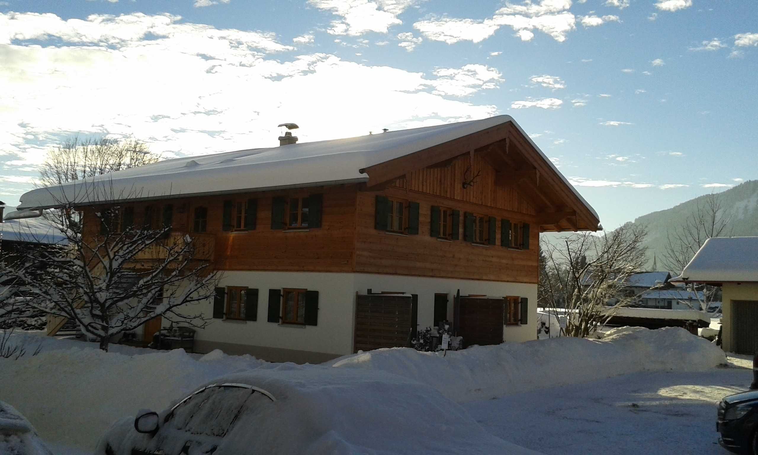 Eine zweigeschossige Holzhütte mit geneigtem Dach, großen Fenstern und einer verschneiten Auffahrt.