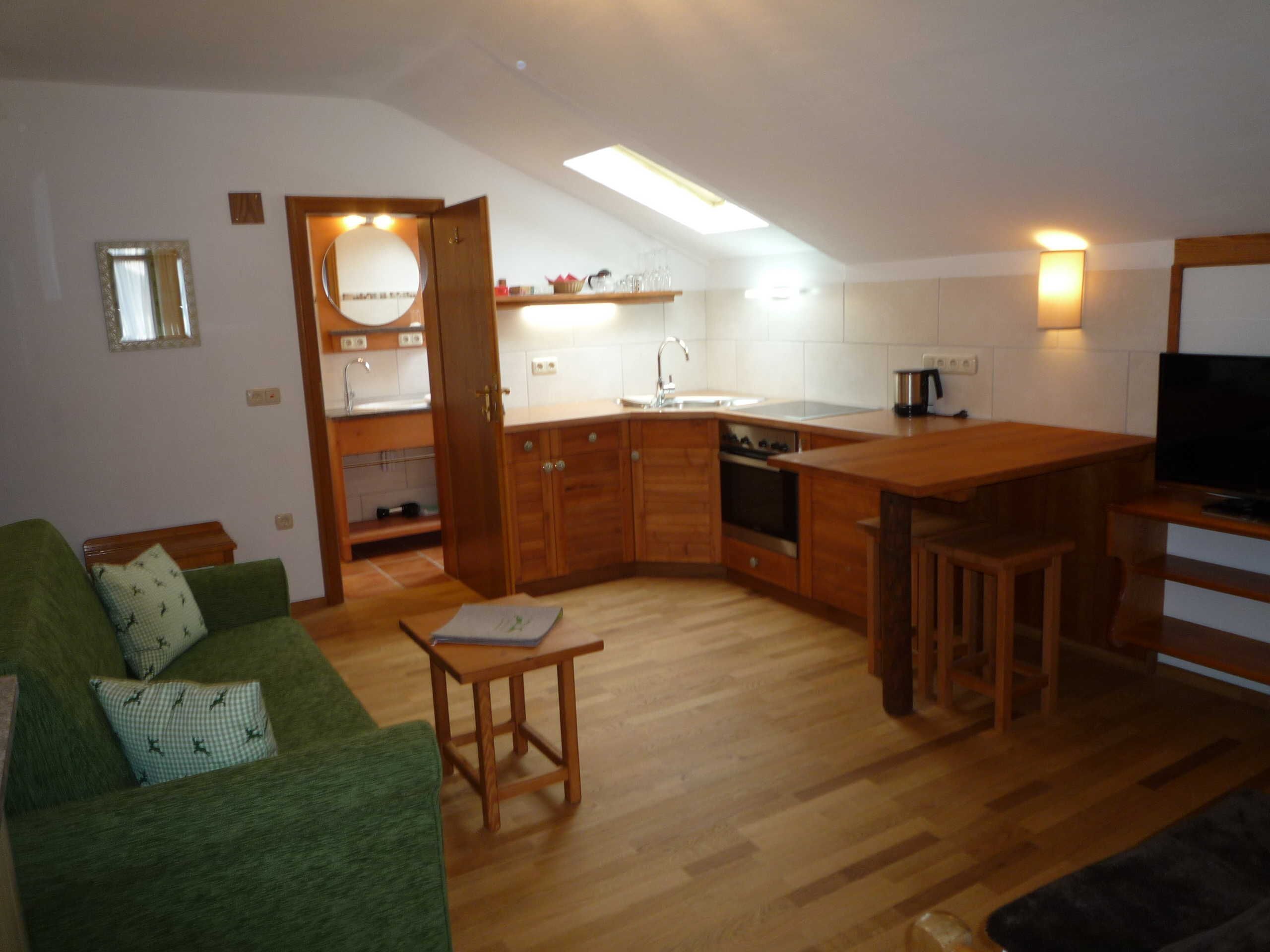Un espacio habitable compacto con kitchenette, un sofá verde, una mesa de comedor de madera y un televisor.