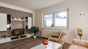 Una sala de estar moderna con un televisor de pantalla plana, armarios blancos, una planta en maceta, un sofá y una mesa de centro con una revista.