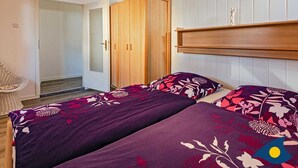 Un dormitorio con dos camas, un armario de madera, una lámpara colgante y una silla de mimbre.