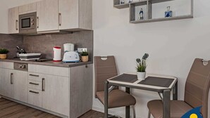 Una cocina compacta con electrodomésticos modernos, una zona de comedor con dos sillas y un pequeño estante con adornos.