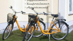 Two bicycles parked in front of a building with a sign listing amenities such as a double room, a comfort room, and apartments. - 2-room apartment - Strandvilla Ostpreussen (Heringsdorf)