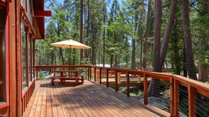 A wooden deck with a picnic table and umbrella, surrounded by tall trees.