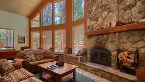 A cozy living room with a stone fireplace, large windows, and comfortable seating.