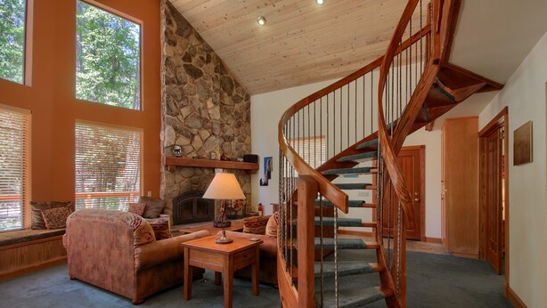 A spacious living room with a stone wall, a wooden staircase, and a fireplace.