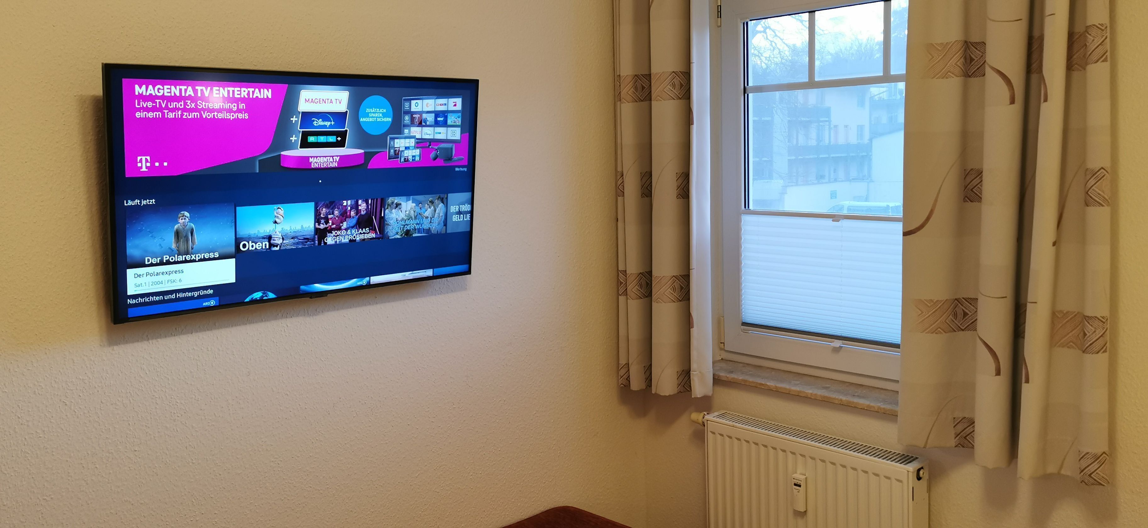 Un televisor de pantalla plana montado en la pared, mostrando la interfaz de un servicio de streaming con varios canales y opciones.
