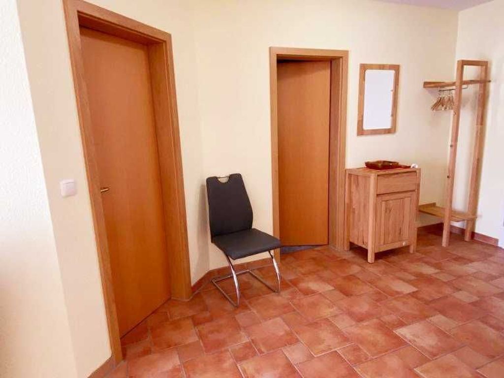 Une pièce avec deux portes en bois, une chaise, un petit meuble en bois et un miroir accroché au mur.